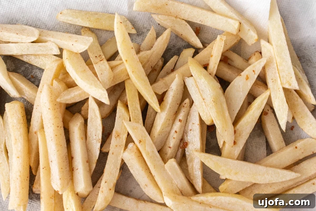 par-fried French fries on a parchment-lined baking sheet, lightly golden