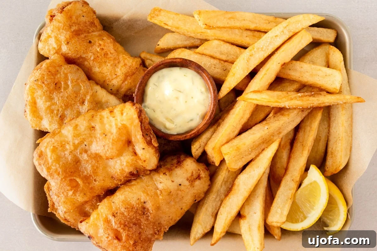 Crispy battered gluten-free fish surrounded by golden fries on a parchment-lined tray with a ramekin of tartar sauce.