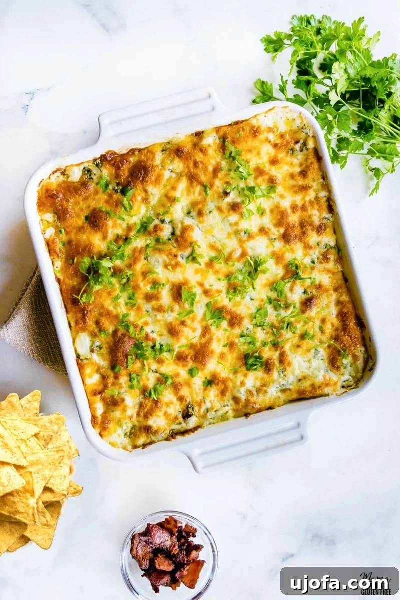 spinach dip in a white baking dish with corn chips, chopped bacon, and parsley on the side