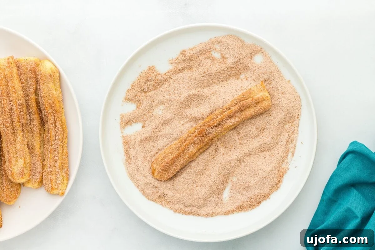 Delectable Gluten-Free Churros 12 A single gluten-free churro being rolled in cinnamon sugar on a plate, with several already coated churros visible beside it.