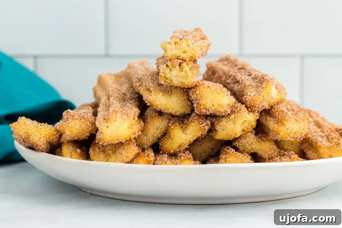 Delectable Gluten-Free Churros 14 A close-up view of a stack of gluten-free churros on a plate, with one churro bitten into to reveal the airy, soft interior and crispy crust.