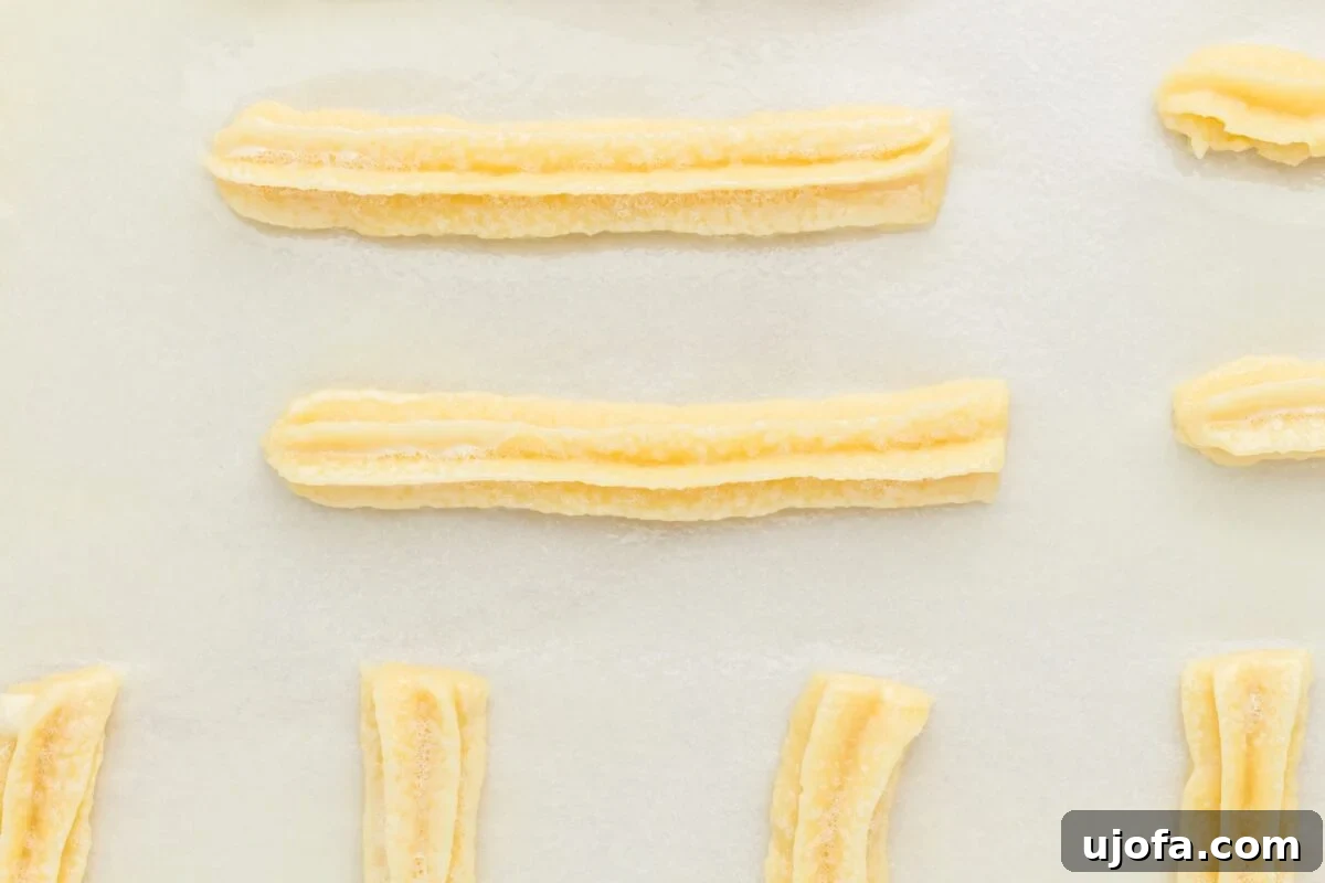Delectable Gluten-Free Churros 10 Freshly baked golden-brown gluten-free churros resting on a parchment-lined baking sheet, having just come out of the oven.