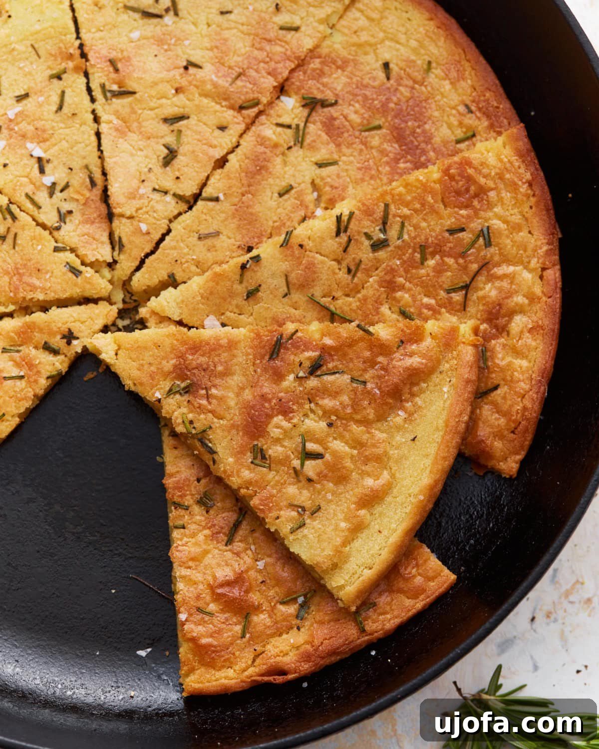 Savory Chickpea Flatbread 2 A sliced farinata (chickpea flatbread) in a cast iron skillet, garnished with rosemary and flaky salt.