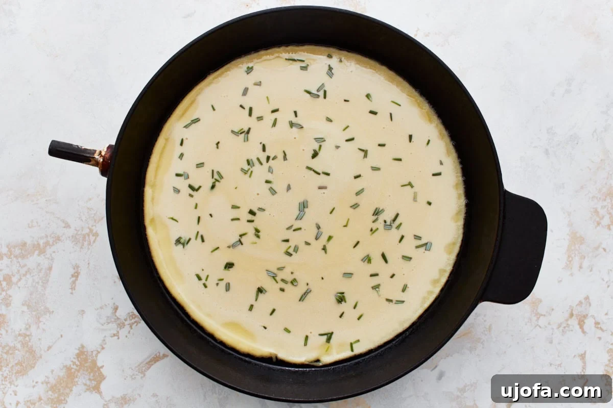 Savory Chickpea Flatbread 11 Uncooked chickpea batter in a skillet, sprinkled with chopped rosemary.