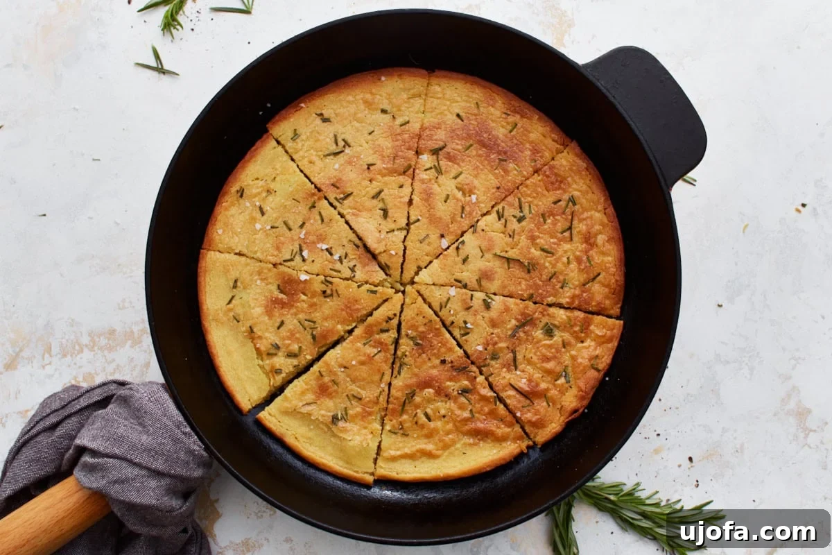 Savory Chickpea Flatbread 13 Farinata in a cast iron skillet, sliced and ready to serve, with rosemary sprigs as decoration.