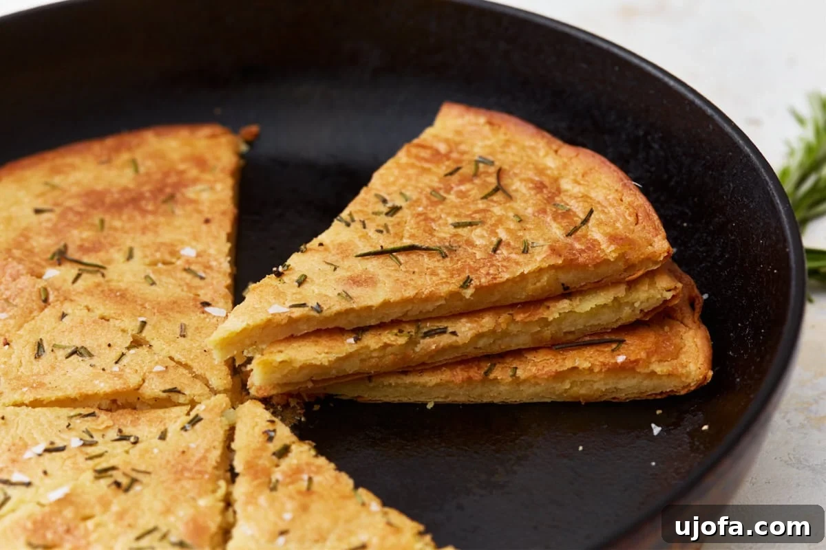 Savory Chickpea Flatbread 14 A side view of sliced farinata stacked in a cast iron skillet, showcasing its texture and golden crust. Topped with fresh rosemary and sea salt.