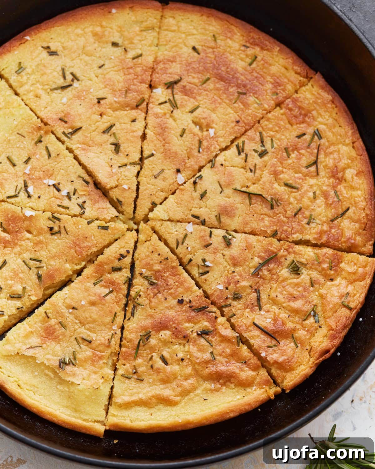 Savory Chickpea Flatbread 4 A top view of a whole farinata in a cast iron skillet, cut into wedges and garnished with rosemary and flaky salt.