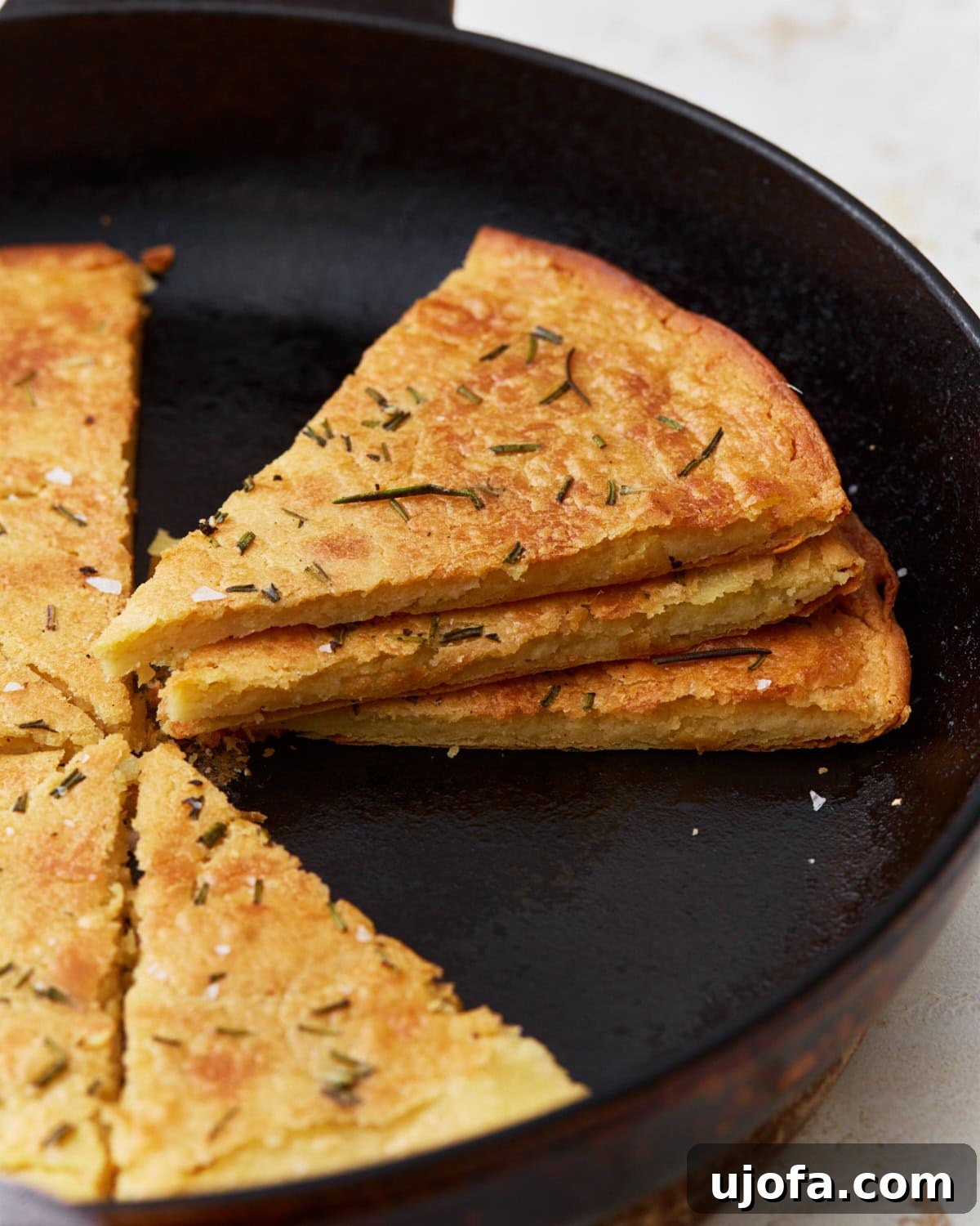 Savory Chickpea Flatbread 5 A side view of sliced farinata stacked in a cast iron skillet, showcasing its texture and golden crust.