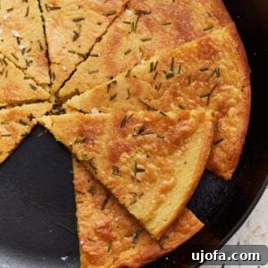 Savory Chickpea Flatbread 6 A sliced farinata (chickpea flatbread) in a cast iron skillet, garnished with rosemary and flaky salt.