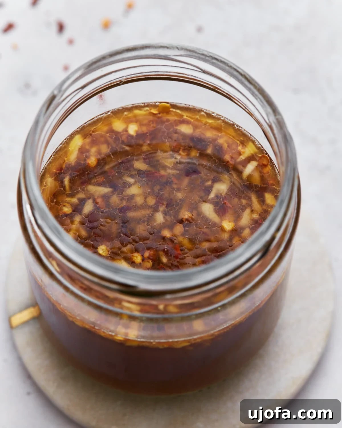 Delicious Gluten-Free Stir Fry Enhancer 9 A top-down view of gluten-free stir-fry sauce in a jar, showcasing its rich brown color with garlic and red chili flakes floating on the surface.