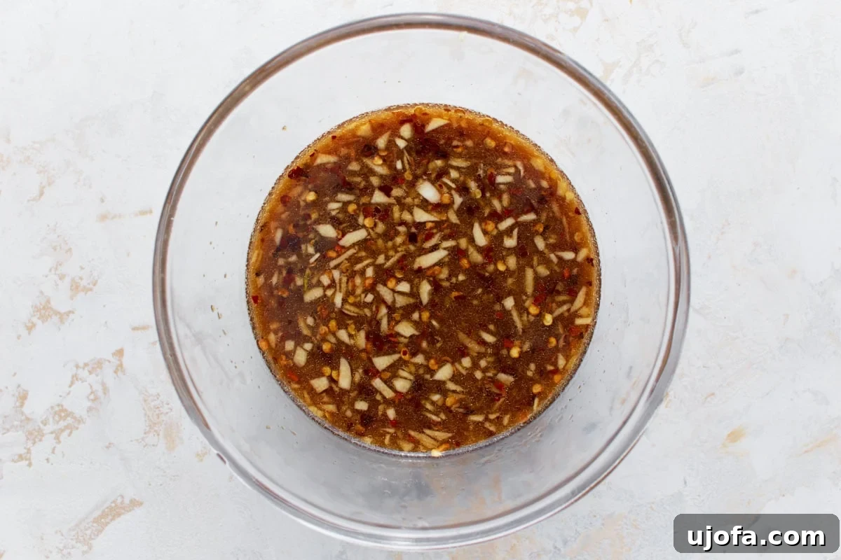 Delicious Gluten-Free Stir Fry Enhancer 6 A clear mixing bowl of gluten-free stir-fry sauce, showing finely chopped garlic, red chili flakes, and a rich texture that enhances its appearance.