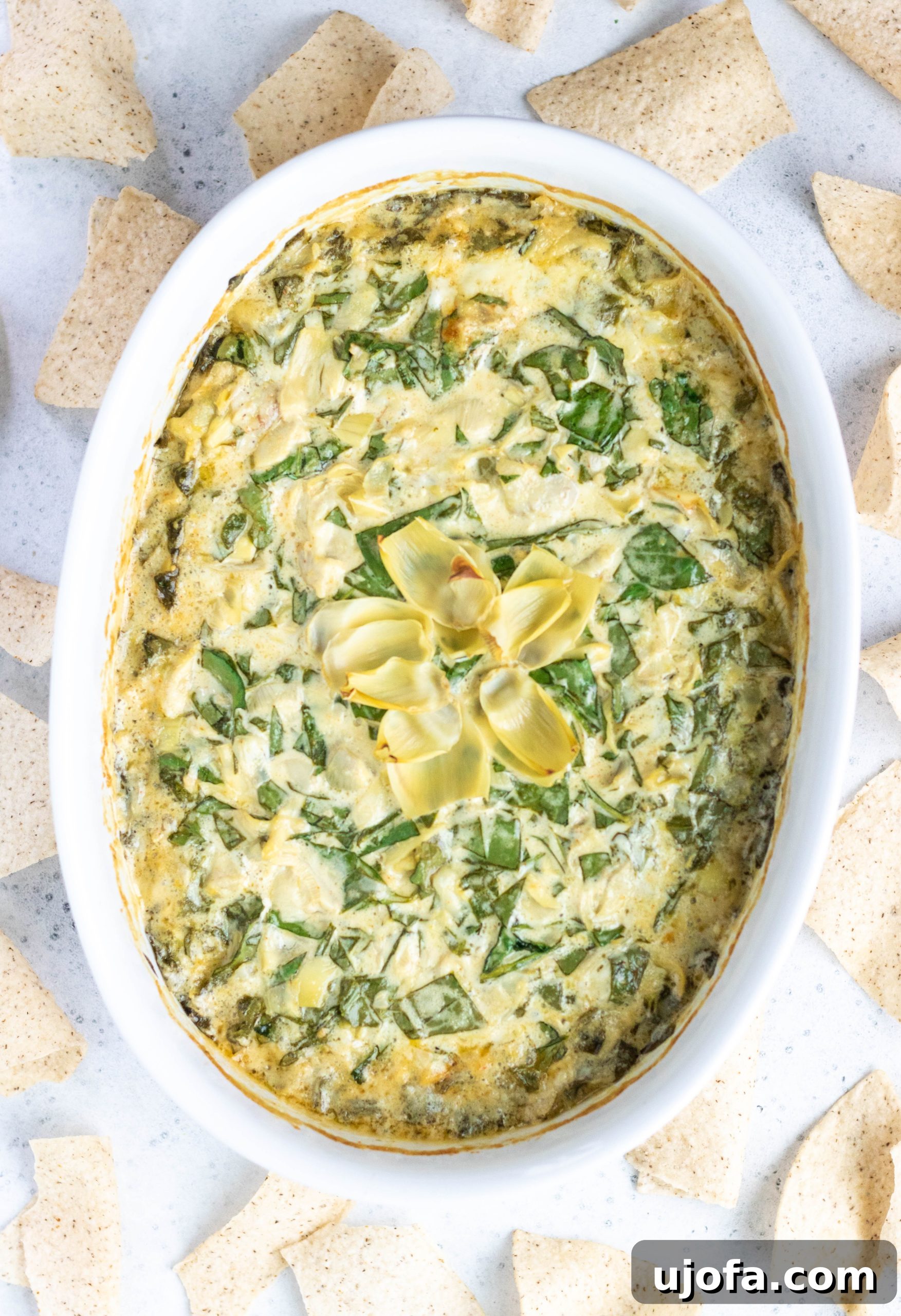 A delectable dairy-free spinach artichoke dip, served in a round casserole dish, artfully surrounded by crispy tortilla chips, ready for dipping.