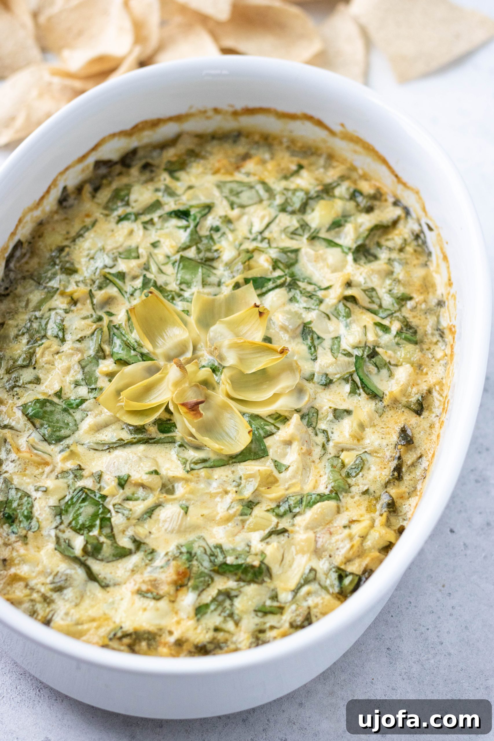 A close-up shot of creamy dairy-free spinach artichoke dip in a round casserole dish, showcasing its rich texture and vibrant colors.