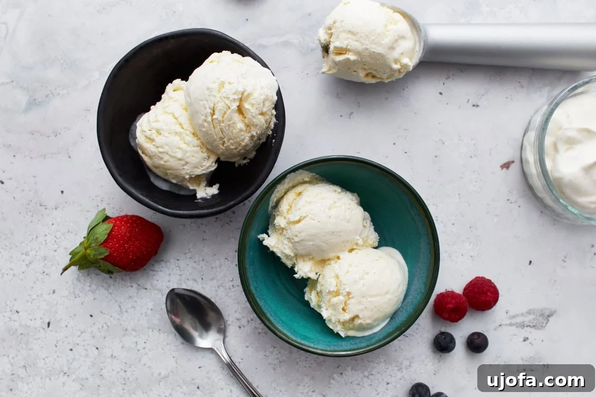 Keto Frozen Delights 12 A teal bowl of keto vanilla ice cream placed next to a scattering of raspberries and blueberries, emphasizing the creamy texture and garnishes.