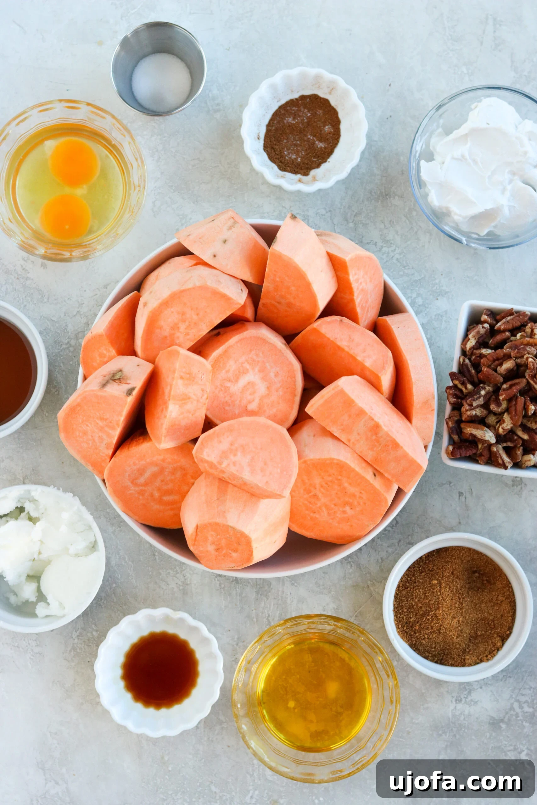 Various healthy ingredients for a paleo and healthier sweet potato casserole, including whole sweet potatoes, pecans, coconut milk, and coconut sugar, laid out on a kitchen counter.
