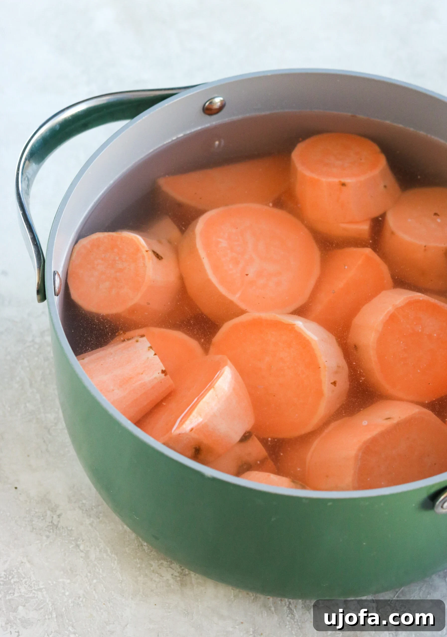 Peeled and uniformly cut sweet potato chunks boiling in a pot of water on a stove, a crucial step in preparing the casserole base.