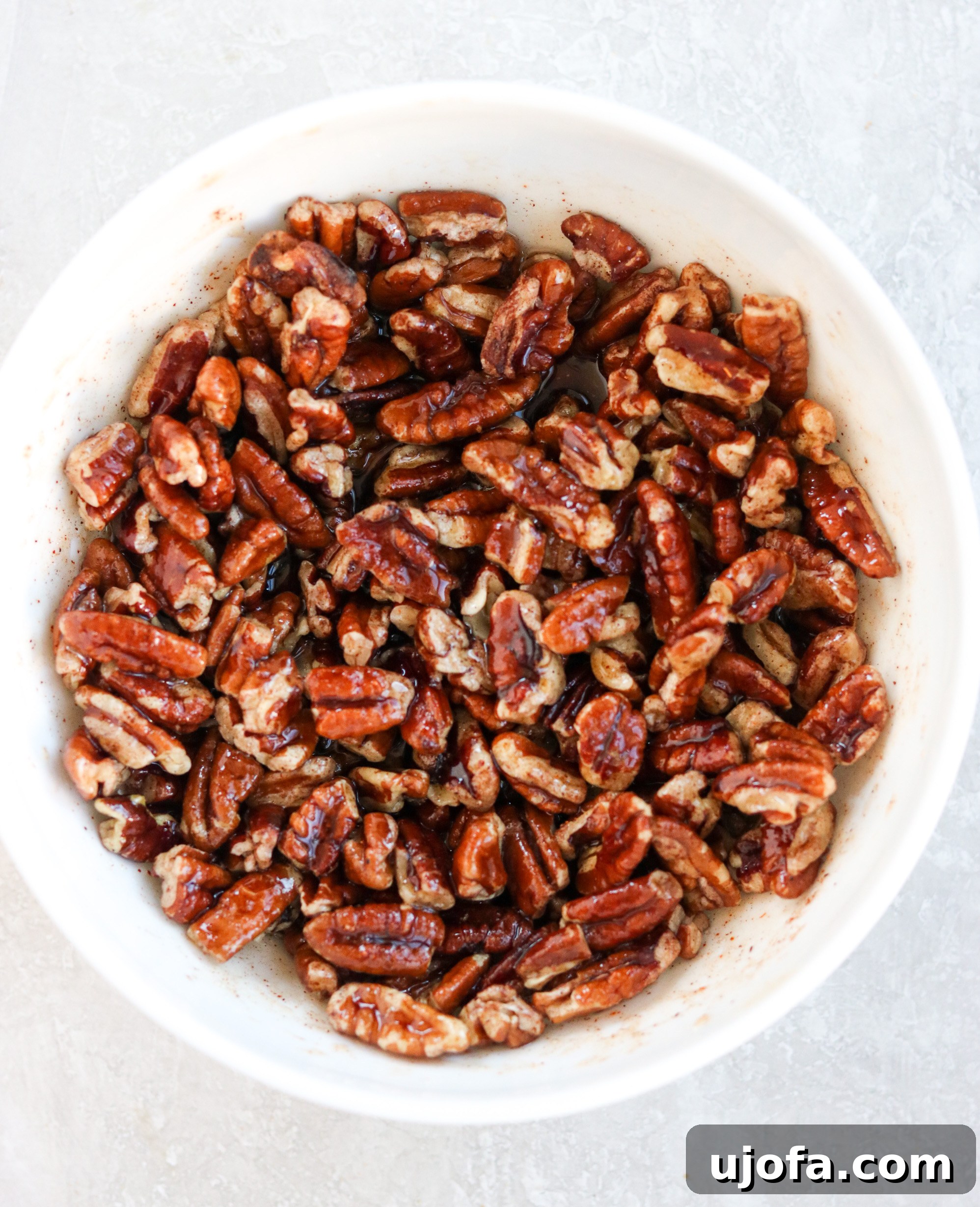 A close-up shot of the maple cayenne pecan topping mixture in a white bowl, showcasing the chopped pecans coated with syrup and spices, ready to be spread over the casserole.