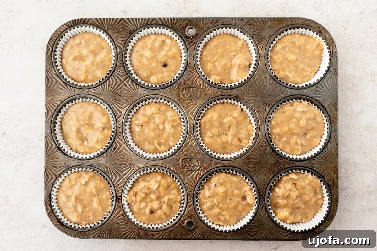 Overhead view of a vintage muffin tin filled with banana oatmeal muffin batter, portioned into paper liners, ready for baking.