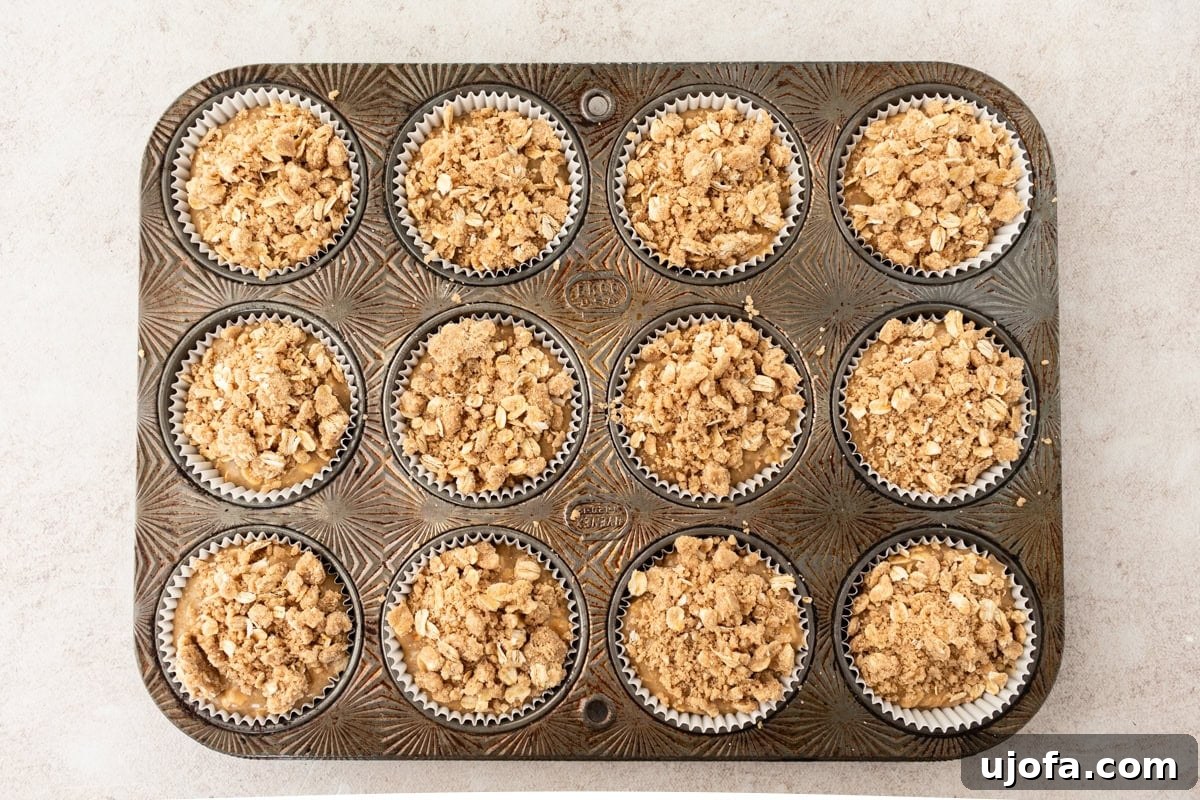 Overhead view of a muffin tin filled with banana oatmeal muffin batter, topped generously with crumbly oat streusel, ready for baking.