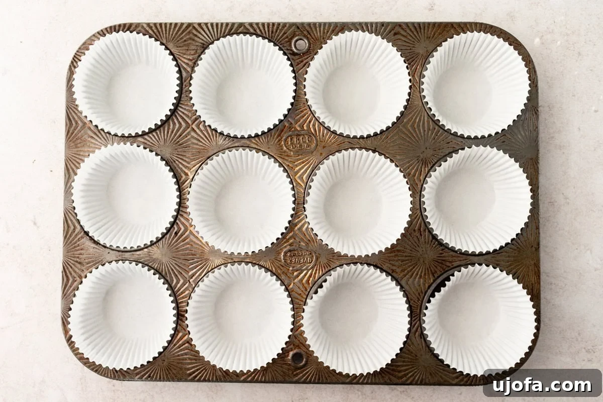 Overhead view of an empty vintage muffin tin lined with white paper liners, ready for baking.