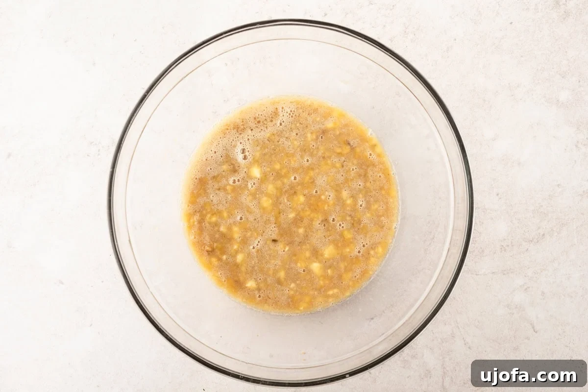 A glass bowl of mashed bananas mixed with wet ingredients, ready to be incorporated into the muffin batter.