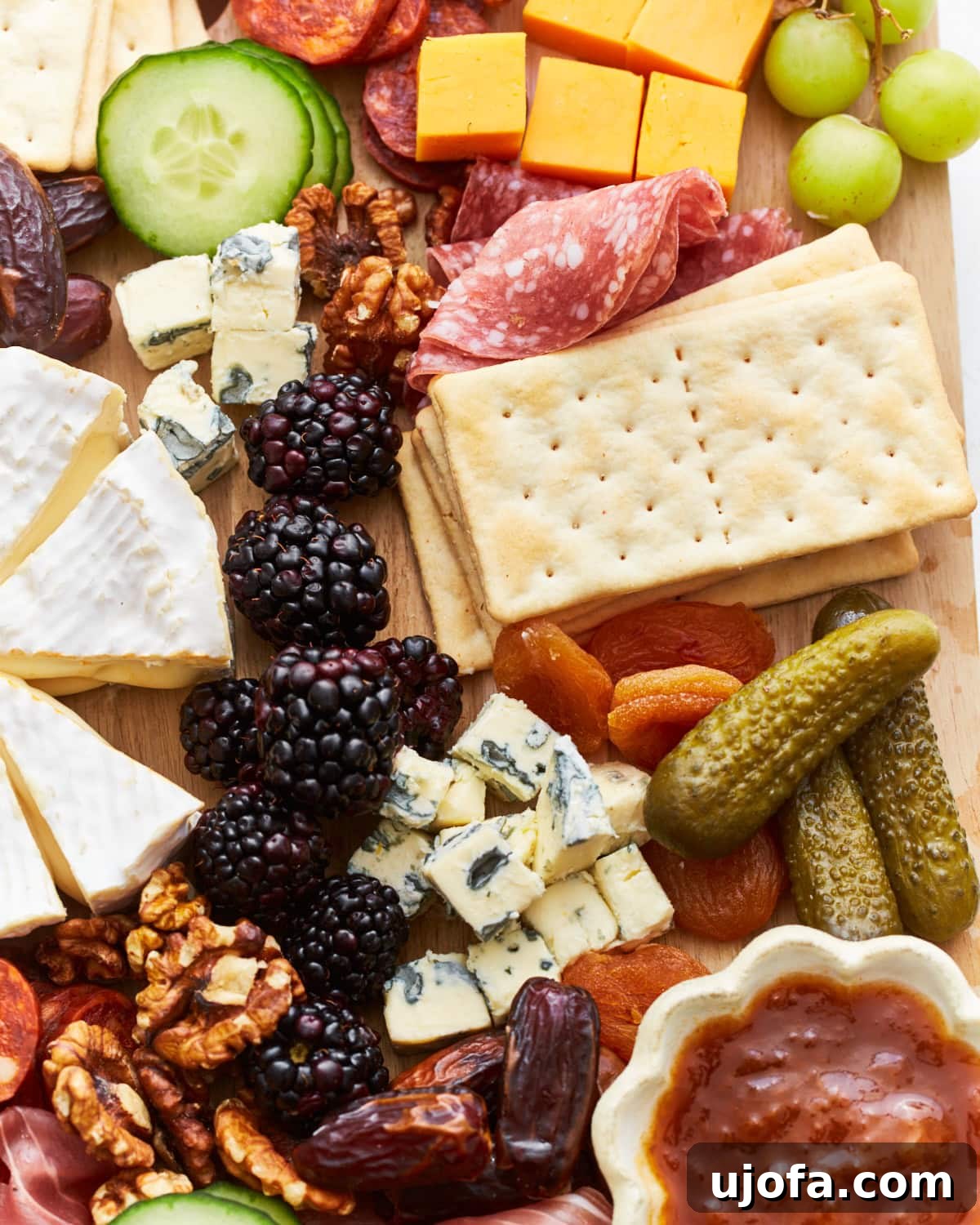 Gourmet Gluten-Free Charcuterie 4 A close-up view of a charcuterie board showcasing creamy Brie, sliced cheddar cubes, blue cheese chunks, dried apricots, dates, fresh blackberries, and crackers. The vibrant colors and textures of the food items are highlighted.