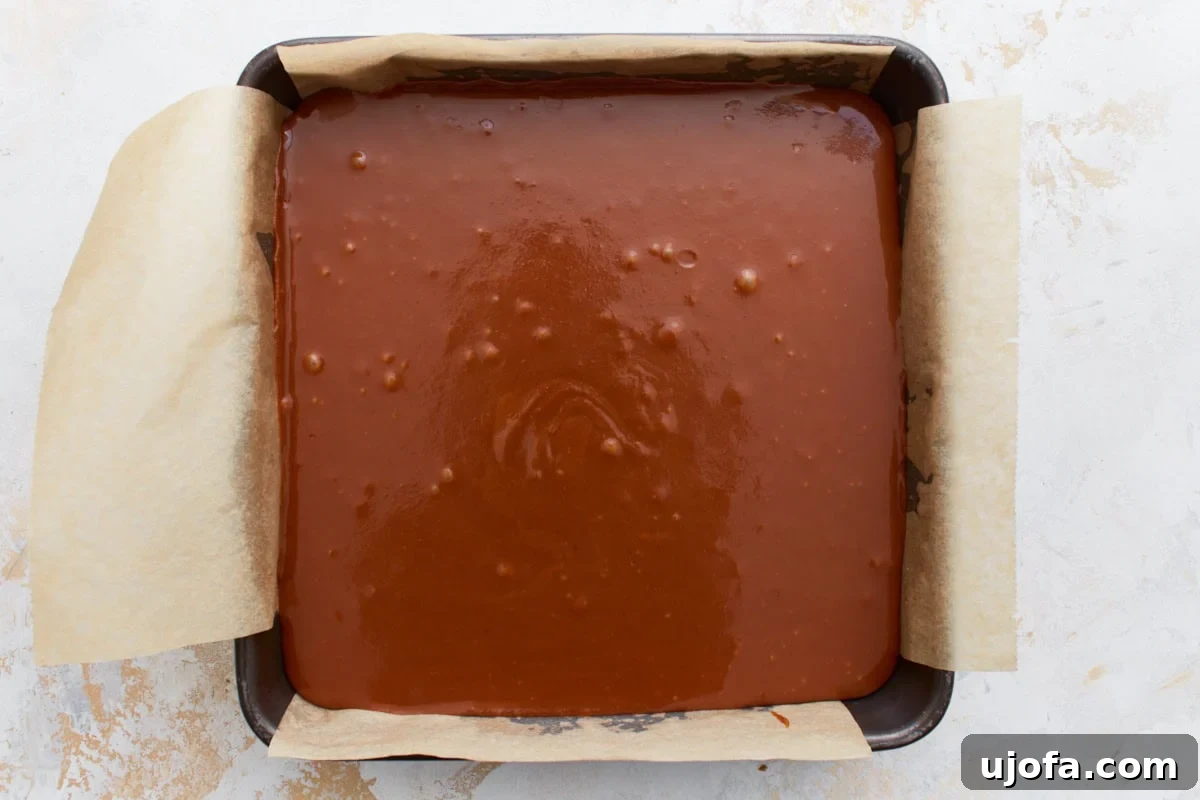A parchment-lined baking pan filled with a smooth layer of caramel, setting atop the baked shortbread base.
