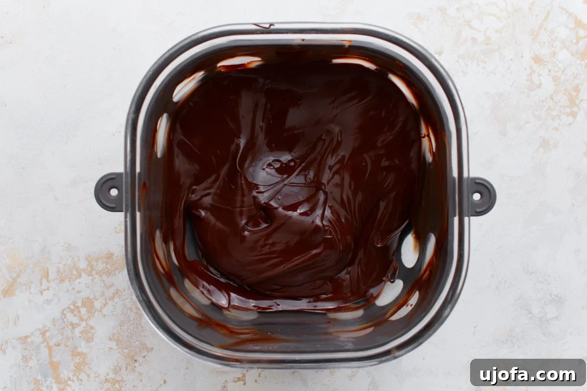 A metal bowl filled with melted glossy chocolate, smooth and ready for spreading over the dessert.