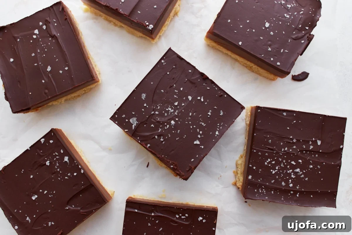 Overhead view of sliced gluten-free millionaire shortbread pieces arranged on parchment paper, each sprinkled with flaky sea salt.