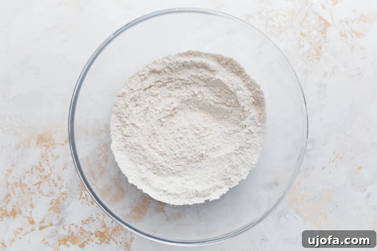 A glass mixing bowl filled with sifted gluten-free flour mixture for the shortbread base, set on a lightly textured surface.