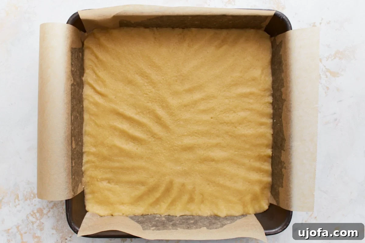 A baking pan lined with parchment paper, filled with evenly spread gluten-free shortbread dough before baking.