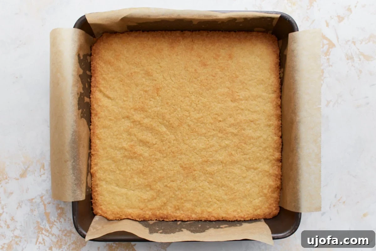 The baked gluten-free shortbread base, golden brown and evenly baked, in a parchment-lined pan.