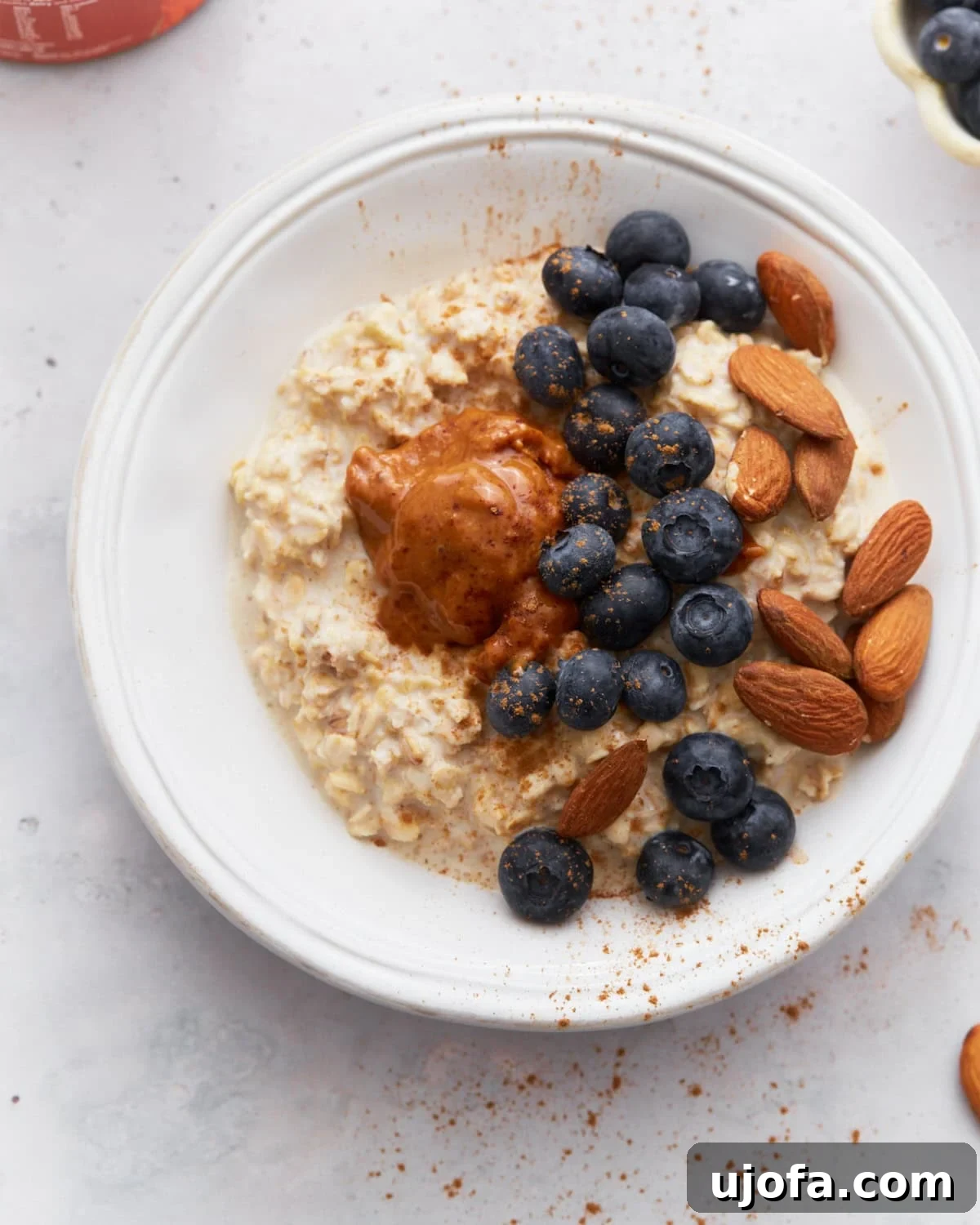 Gluten-Free Overnight Oats: Prep Today, Enjoy Tomorrow 2 A bowl of creamy gluten-free overnight oats topped with fresh blueberries, whole almonds, and a dollop of almond butter, sprinkled with cinnamon, on a light surface.