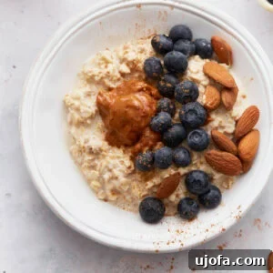 A bowl of creamy gluten-free overnight oats topped with fresh blueberries, whole almonds, and a dollop of almond butter, sprinkled with cinnamon, on a light surface.
