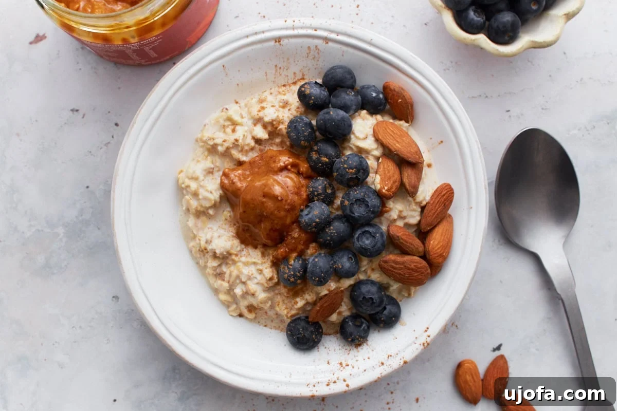 Gluten-Free Overnight Oats: Prep Today, Enjoy Tomorrow 8 A top view of a beautifully arranged bowl of gluten-free overnight oats with blueberries, almonds, almond butter, and a sprinkle of cinnamon, alongside a spoon and additional toppings scattered around.