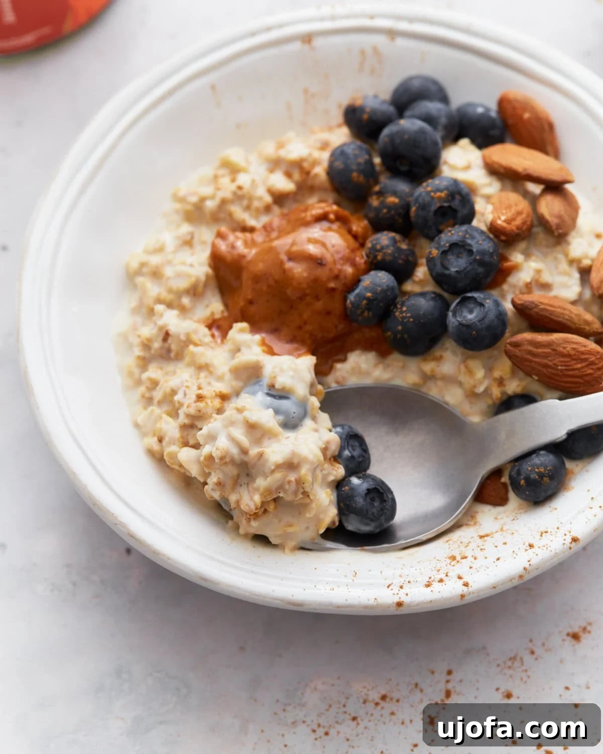 Gluten-Free Overnight Oats: Prep Today, Enjoy Tomorrow 9 A close-up of gluten-free overnight oats with toppings, including blueberries, almonds, and almond butter, with a spoon scooping up a bite.
