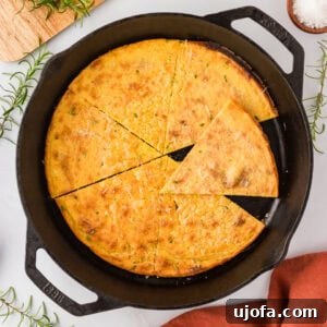 A golden-brown socca flatbread baked in a cast iron skillet, cut into triangular slices, garnished with fresh rosemary and grated cheese.
