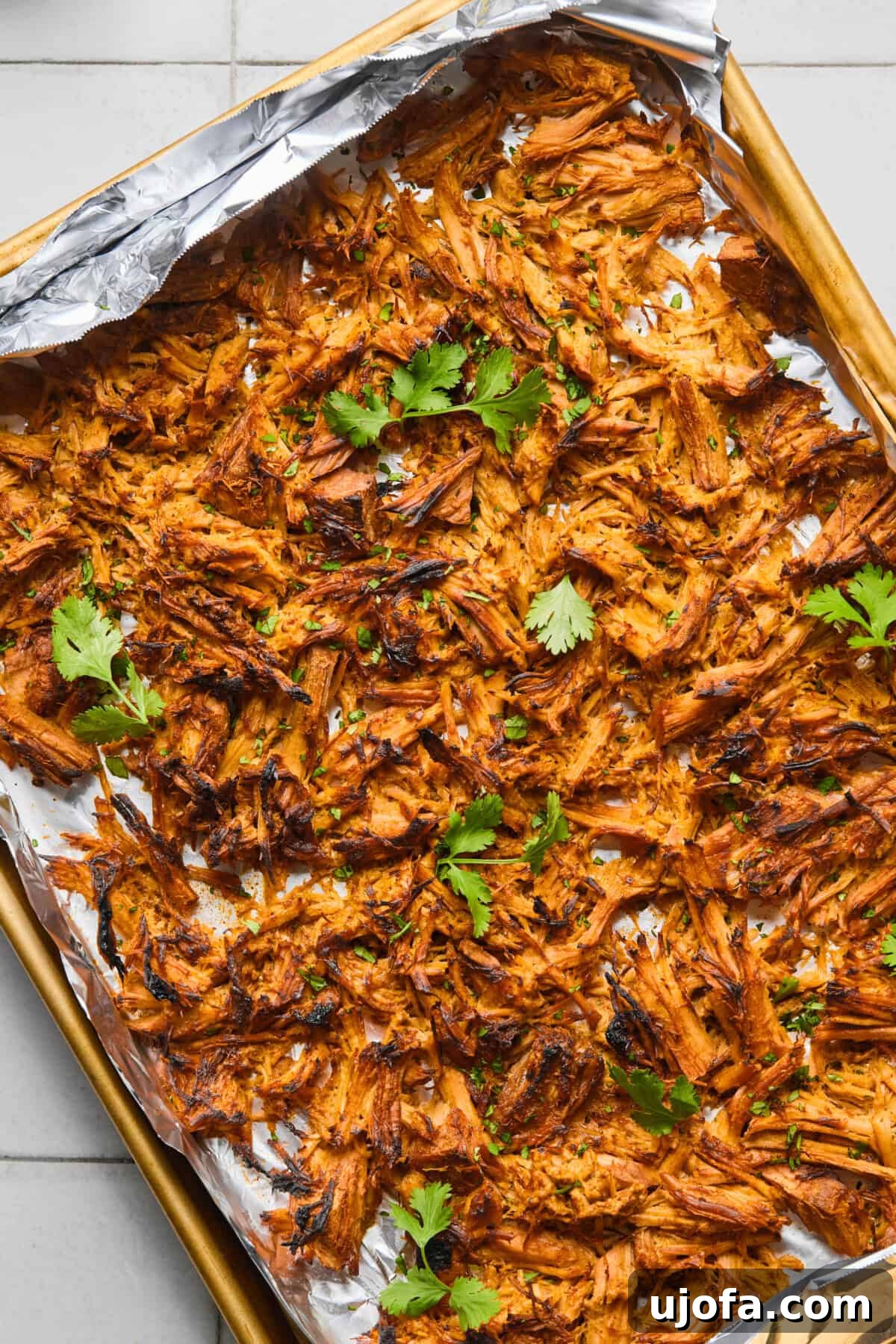 Crispy shredded pork carnitas on a foiled lined baking sheet, garnished with fresh cilantro sprigs