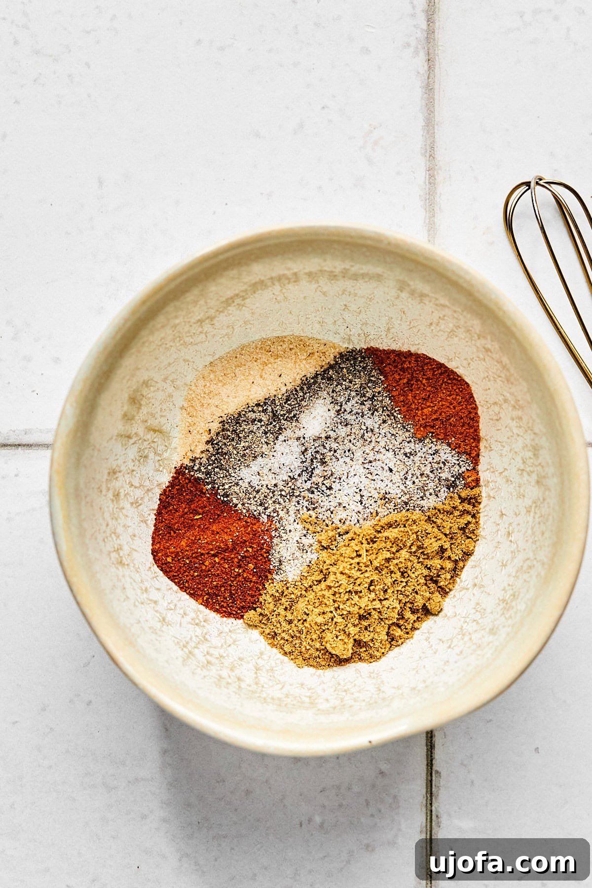 Small bowl containing a vibrant spice rub mixture, featuring ground cumin, chili powder, and red cayenne pepper, ready to season the pork