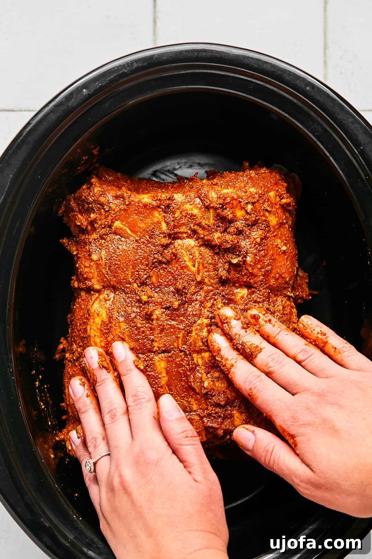 Raw pork roast, generously coated with a rich spice mixture, positioned neatly inside a slow cooker, ready for cooking