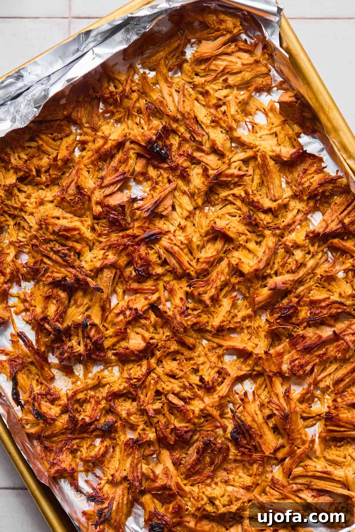 Golden brown, crispy shredded pork carnitas spread evenly on a foil-lined baking sheet, glistening after being broiled to perfection