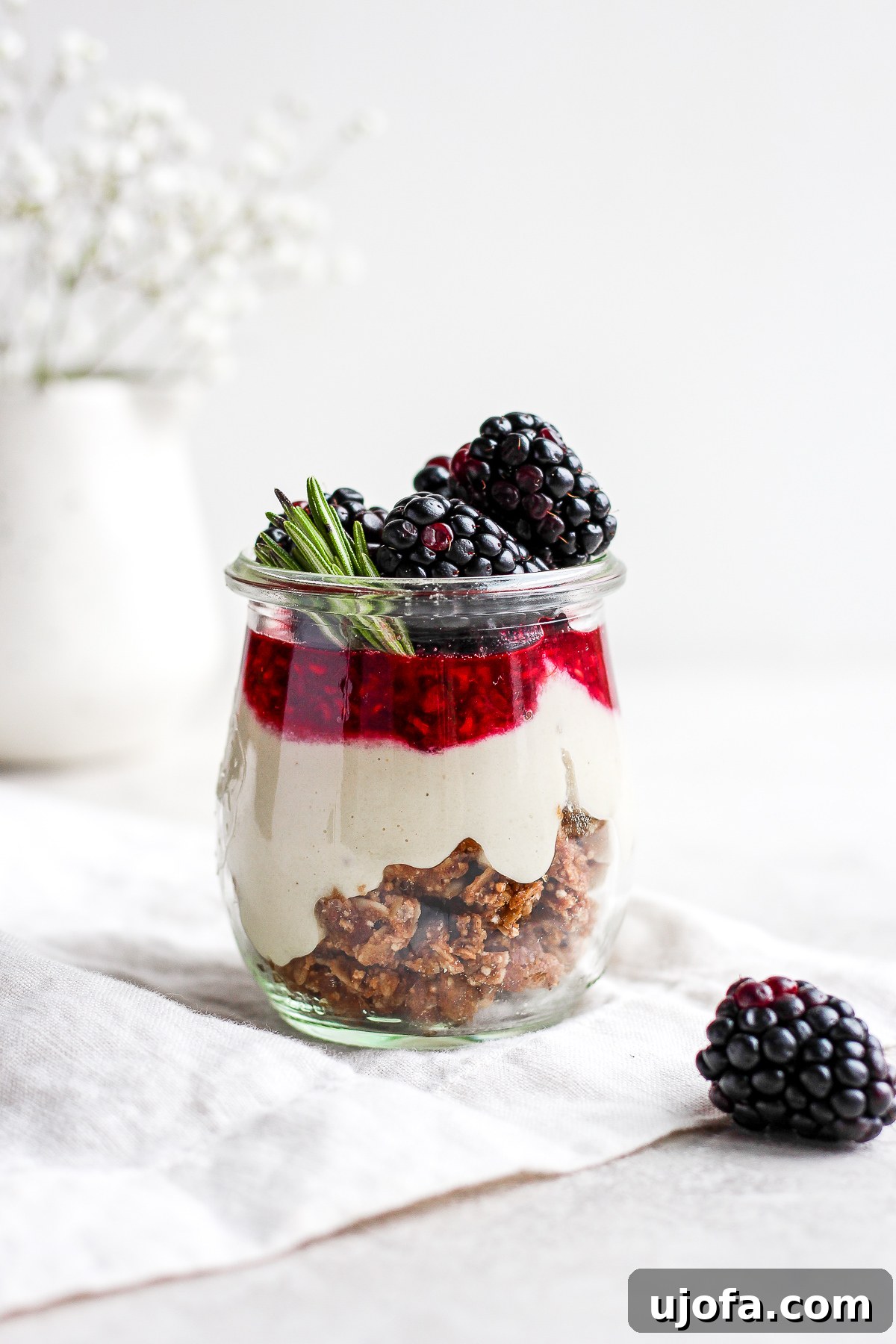 Individual serving jars filled with layered vegan and paleo blackberry cheesecake, garnished with fresh berries.