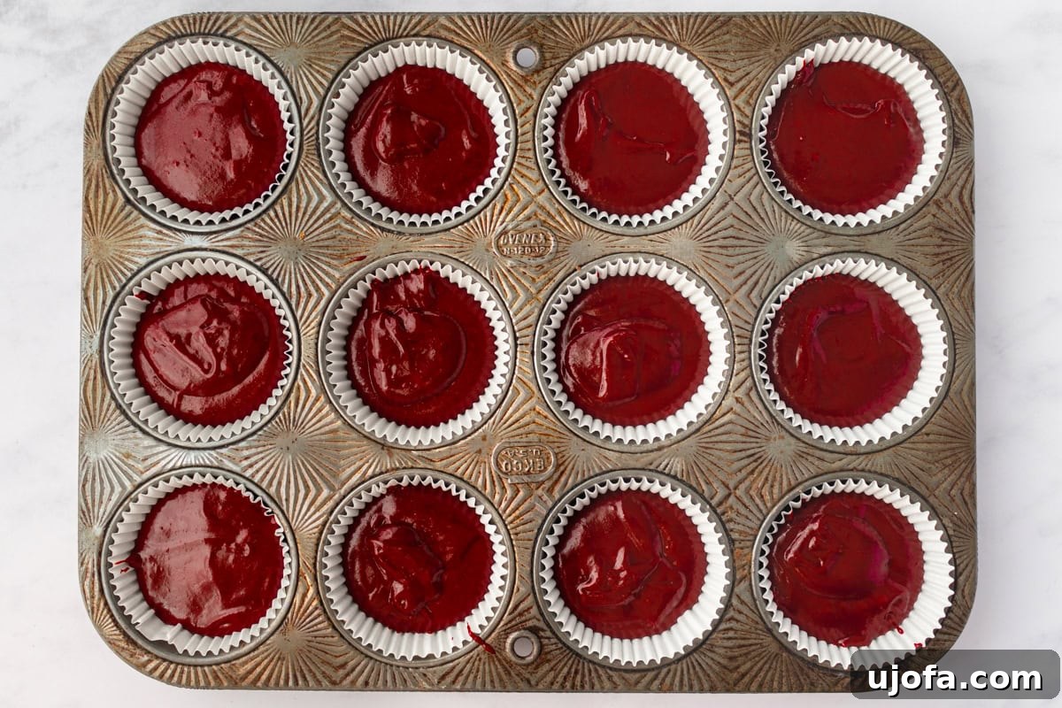 Cupcake pan filled with red velvet batter, lined with white cupcake liners, ready to be baked.