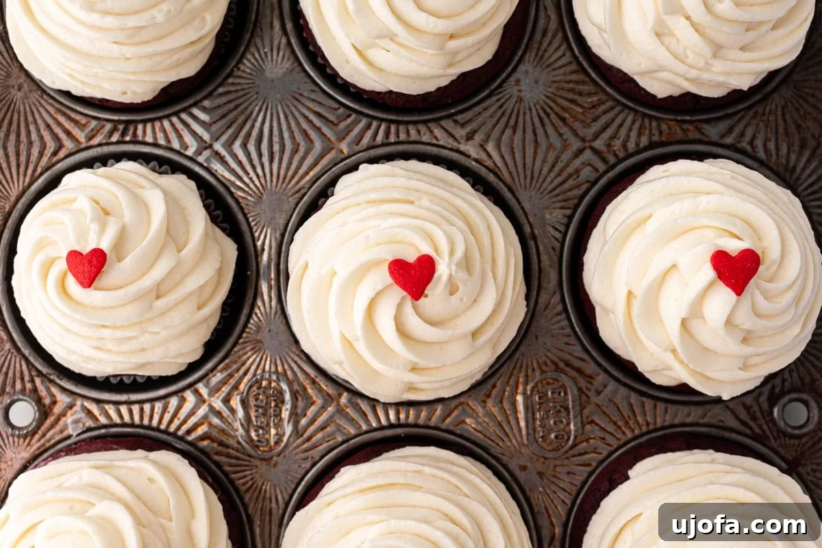 Overhead shot of gluten-free red velvet cupcakes in a vintage muffin tin, topped with swirled cream cheese frosting and small red heart decorations.