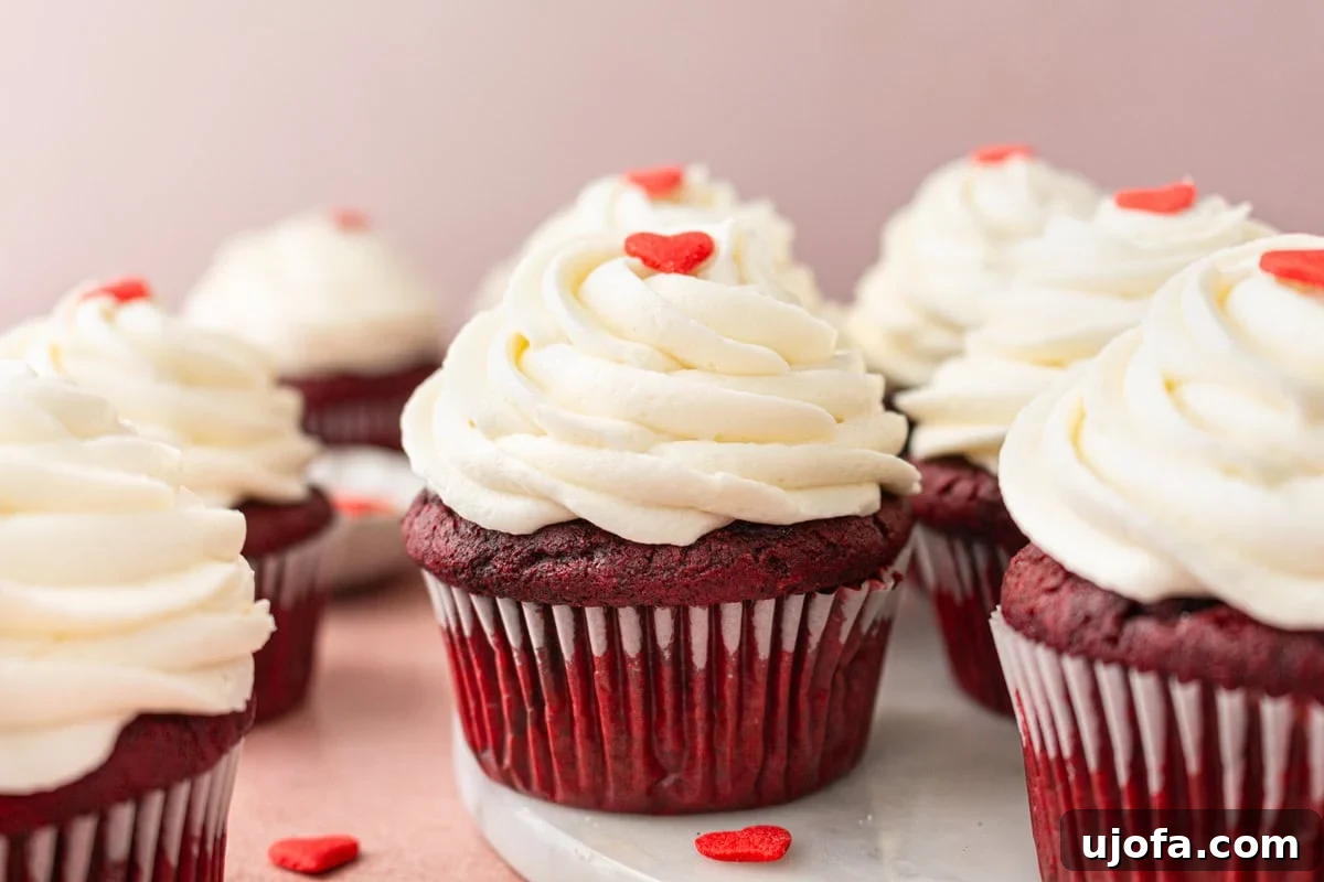 Close-up of gluten-free red velvet cupcakes on a marble serving board, with fluffy cream cheese frosting piped in elegant swirls and red heart sprinkles for decoration.