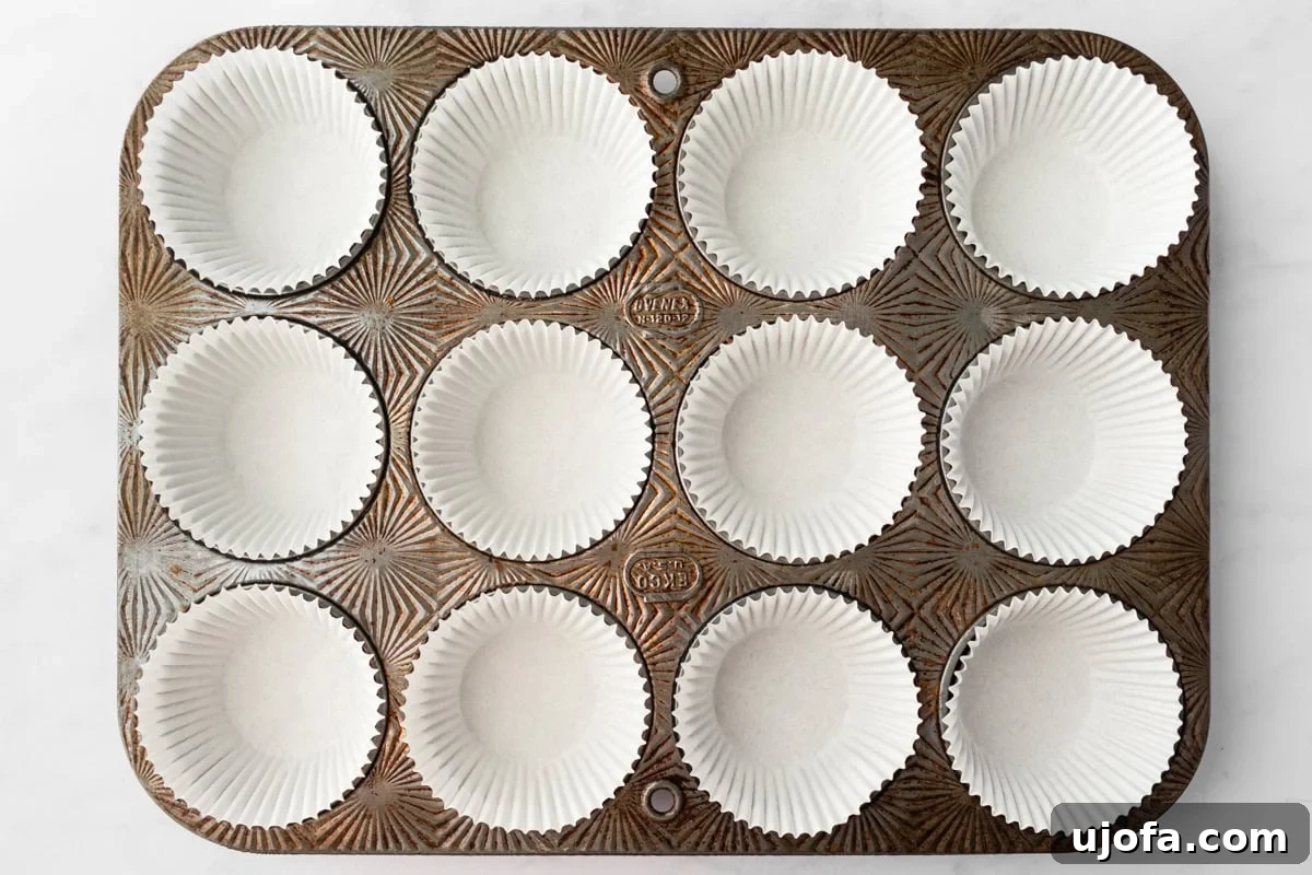 Empty cupcake pan lined with white paper liners, placed on a white surface. The pan has a vintage, textured look.
