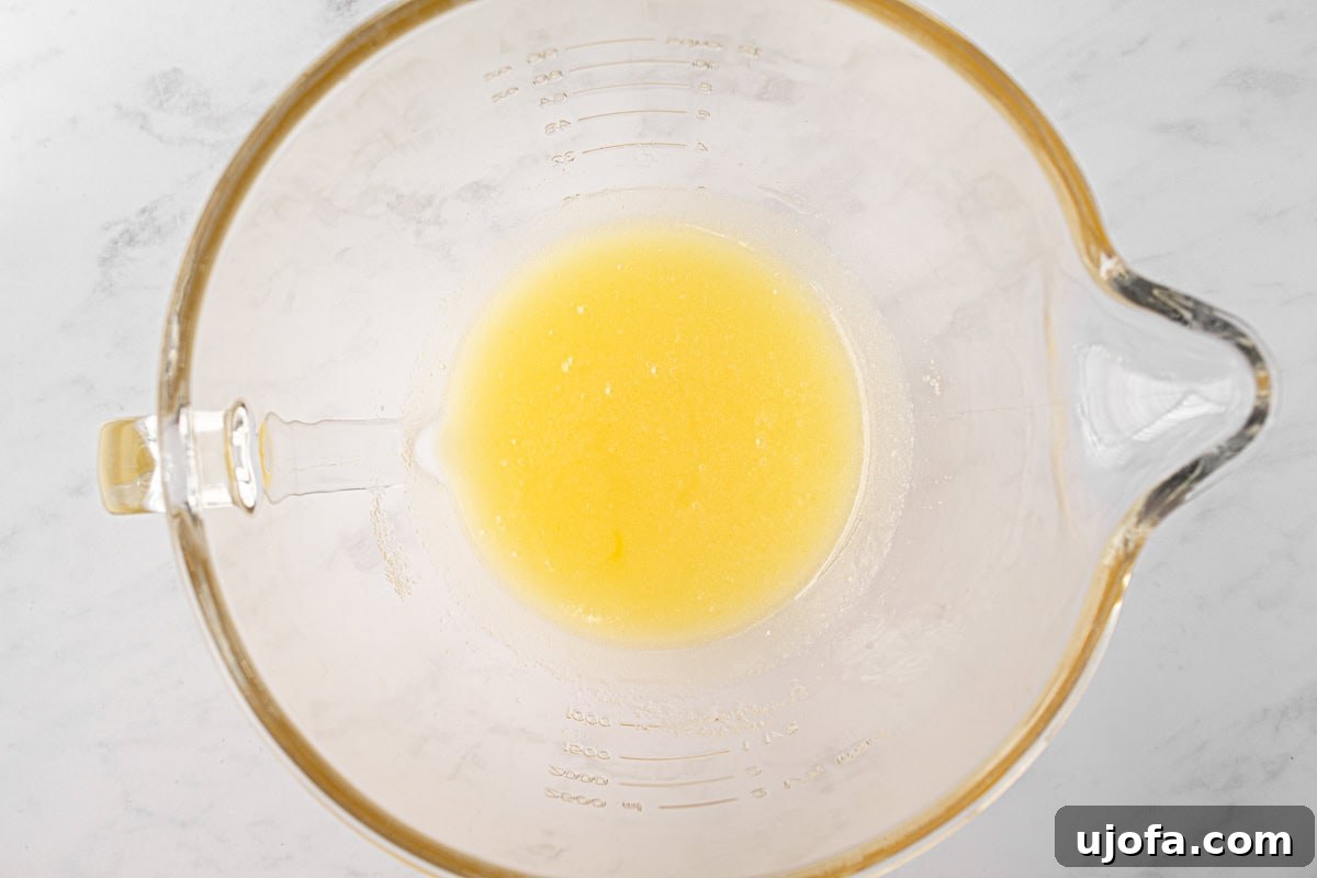 A glass mixing bowl with beaten oil and sugar, showing a smooth, pale yellow mixture.