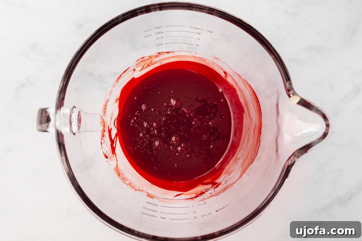 A glass mixing bowl with bright red liquid batter, after adding red food coloring and vanilla extract.