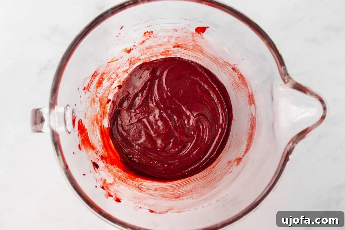 A glass mixing bowl with thick red velvet cupcake batter, well combined and ready for baking.