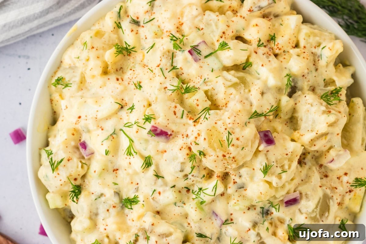 A top-down view of a gluten-free potato salad, showcasing vibrant colors from the red onions, fresh dill, and creamy dressing.